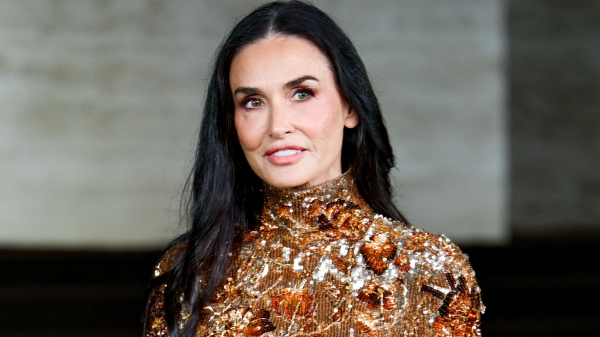 Demi Moore wears an ornate highnecked gown in shades of bronze and copper. Her hair is worn long and loose.